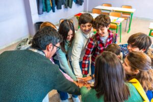 Students and teachers joining hands in classroom, showing teamwork and collaboration