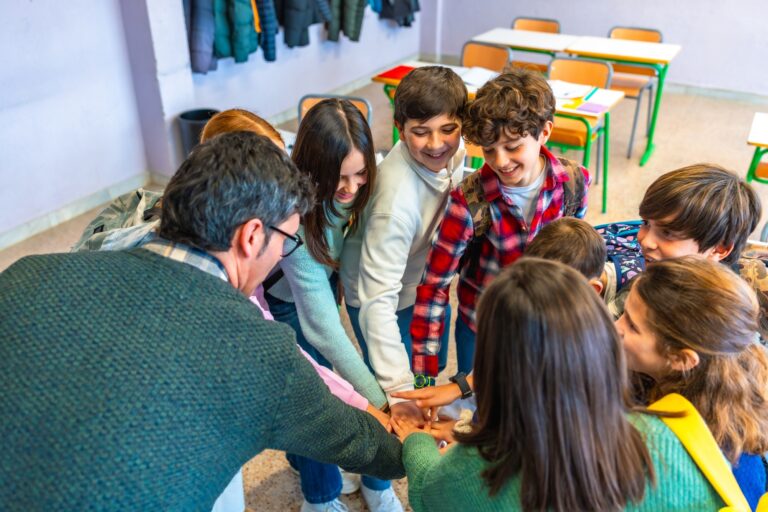 Students and teachers joining hands in classroom, showing teamwork and collaboration